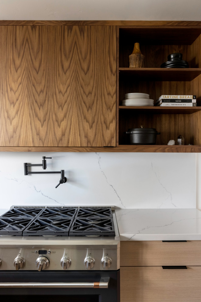 Immagine di una cucina moderna di medie dimensioni con ante lisce, ante in legno chiaro, top in quarzite, paraspruzzi bianco, paraspruzzi in quarzo composito, elettrodomestici neri e top bianco