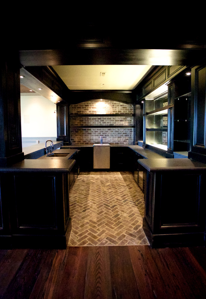 Inspiration for a traditional galley seated home bar in Other with raised-panel cabinets, black cabinets, granite benchtops, brown splashback, stone tile splashback and brick floors.