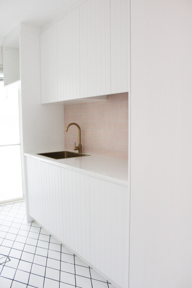 Inspiration for a mid-sized modern single-wall dedicated laundry room in Perth with a drop-in sink, shaker cabinets, white cabinets, quartz benchtops, pink splashback, mosaic tile splashback, white walls, porcelain floors, a stacked washer and dryer, white floor and white benchtop.