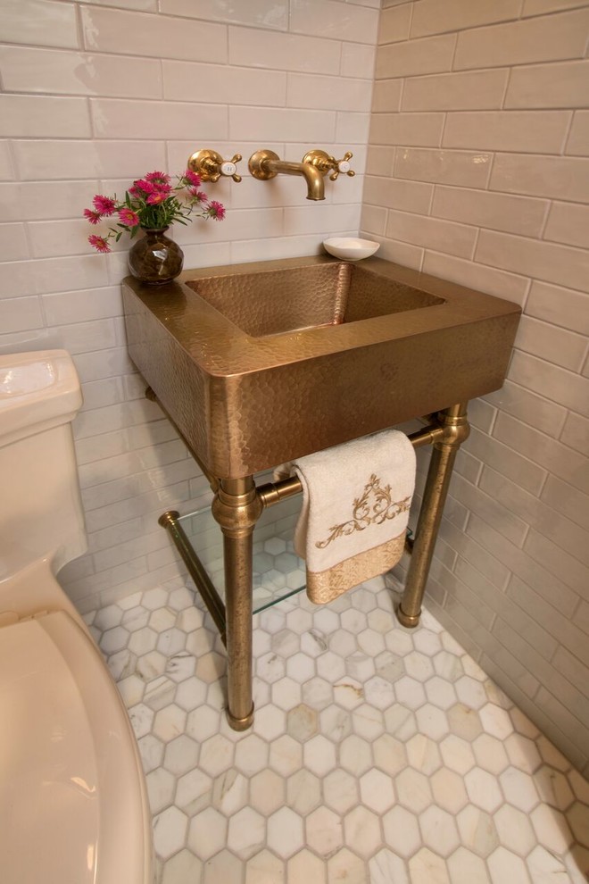 This is an example of a small transitional powder room in New York with a one-piece toilet, beige tile, ceramic tile, beige walls, marble floors, a console sink, multi-coloured floor and open cabinets.