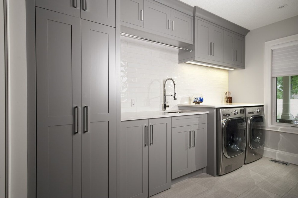 Design ideas for a large contemporary utility room in Toronto with a single-bowl sink, shaker cabinets, grey cabinets, quartz benchtops, grey walls, porcelain floors and a side-by-side washer and dryer.