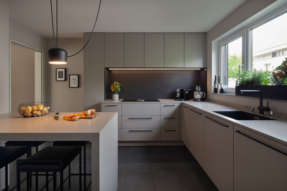 Photo of a large modern l-shaped open plan kitchen in Cologne with an integrated sink, flat-panel cabinets, grey cabinets, solid surface benchtops, black splashback, timber splashback, stainless steel appliances, cement tiles, with island, black floor and grey benchtop.