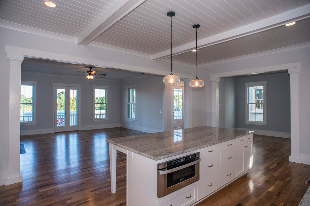 Inspiration for a contemporary l-shaped eat-in kitchen in Charleston with a farmhouse sink, recessed-panel cabinets, white cabinets, granite benchtops, white splashback, ceramic splashback, stainless steel appliances, medium hardwood floors and with island.