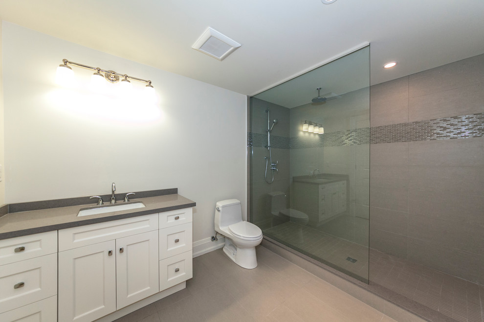 Photo of a large transitional bathroom in Toronto with an undermount sink, a double shower, a one-piece toilet, white cabinets, shaker cabinets, engineered quartz benchtops, gray tile, porcelain tile, white walls and porcelain floors.