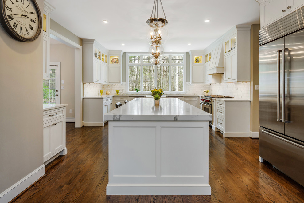 Example of a large transitional u-shaped dark wood floor and brown floor kitchen design in Bridgeport with a farmhouse sink, flat-panel cabinets, white cabinets, quartz countertops, white backsplash, marble backsplash, stainless steel appliances, an island and white countertops