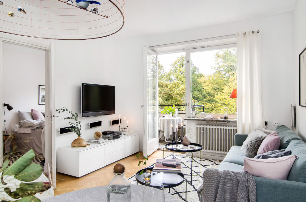 Photo of a mid-sized scandinavian enclosed living room in Stockholm with white walls, light hardwood floors, a wall-mounted tv and no fireplace.