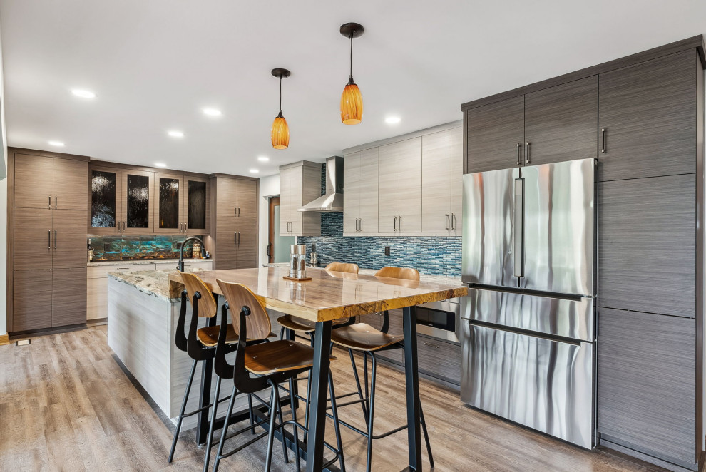 Mid-sized contemporary l-shaped open plan kitchen in Columbus with an undermount sink, flat-panel cabinets, beige cabinets, granite benchtops, blue splashback, glass tile splashback, stainless steel appliances, laminate floors, with island, beige floor and white benchtop.