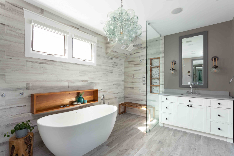 This is an example of a mid-sized contemporary master bathroom in Chicago with furniture-like cabinets, grey cabinets, a freestanding tub, a curbless shower, a two-piece toilet, multi-coloured tile, porcelain tile, beige walls, porcelain floors, a drop-in sink, engineered quartz benchtops, beige floor, an open shower, beige benchtops, a shower seat, a double vanity and a freestanding vanity.