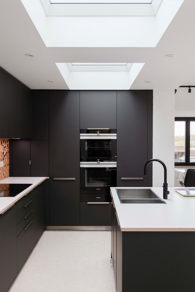 This is an example of a large contemporary l-shaped open plan kitchen in London with black cabinets, wood benchtops, panelled appliances, cork floors, with island, white floor, white benchtop and vaulted.