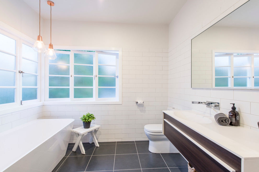 Design ideas for a contemporary bathroom in Brisbane with flat-panel cabinets, dark wood cabinets, a freestanding tub, a two-piece toilet, black tile, white tile, white walls and a wall-mount sink.