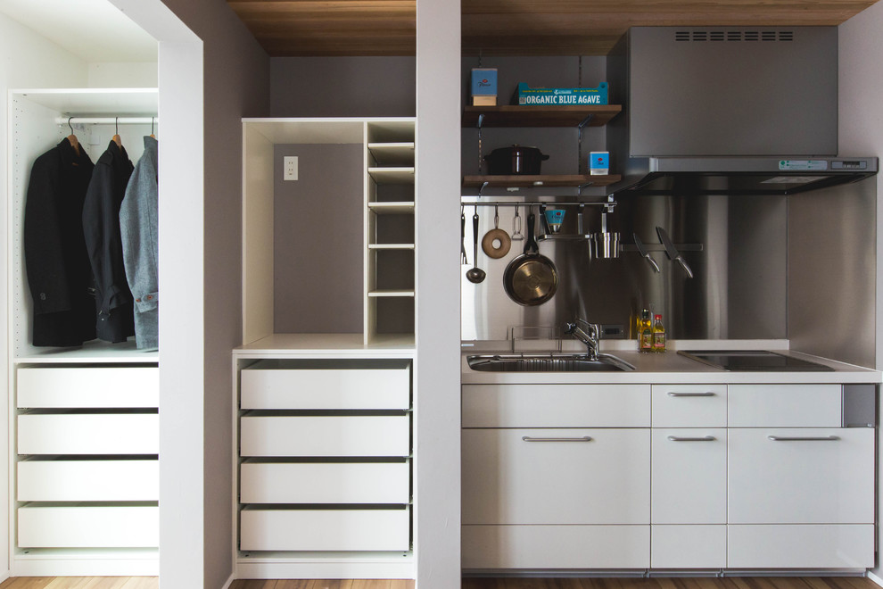 Photo of a small contemporary single-wall kitchen in Kyoto with white cabinets, solid surface benchtops, white splashback, black appliances, plywood floors, a peninsula and brown floor.