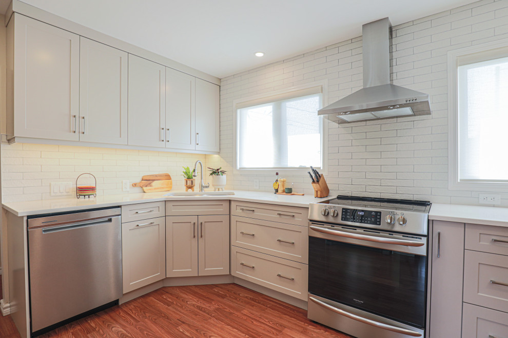 Inspiration for a mid-sized transitional l-shaped vinyl floor and brown floor eat-in kitchen remodel in Edmonton with an undermount sink, shaker cabinets, beige cabinets, quartz countertops, white backsplash, ceramic backsplash, stainless steel appliances, no island and white countertops