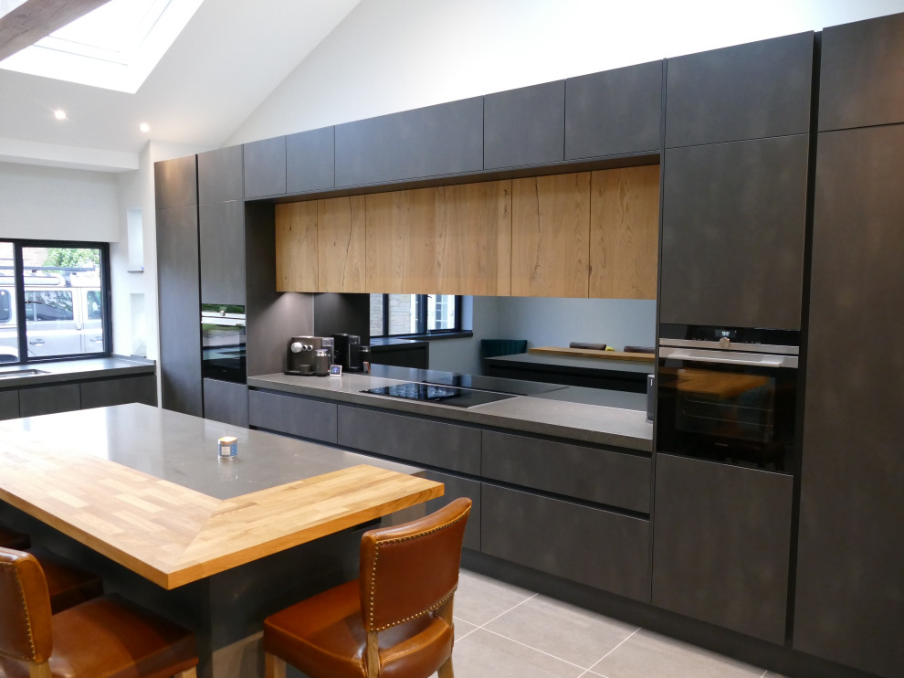 Photo of a large modern single-wall open plan kitchen in Buckinghamshire with an integrated sink, flat-panel cabinets, grey cabinets, quartz worktops, grey splashback, mirror splashback, black appliances, porcelain flooring, an island, grey floors, grey worktops and exposed beams.