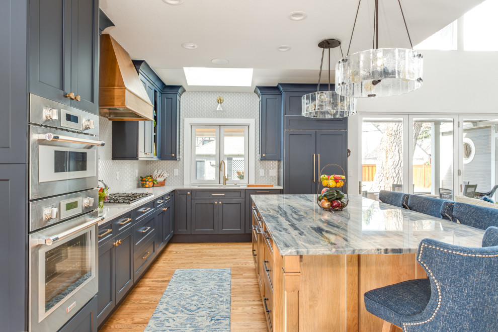 Foto på ett stort vintage blå kök, med en undermonterad diskho, luckor med infälld panel, blå skåp, bänkskiva i kvartsit, vitt stänkskydd, stänkskydd i keramik, integrerade vitvaror, ljust trägolv, en köksö och brunt golv