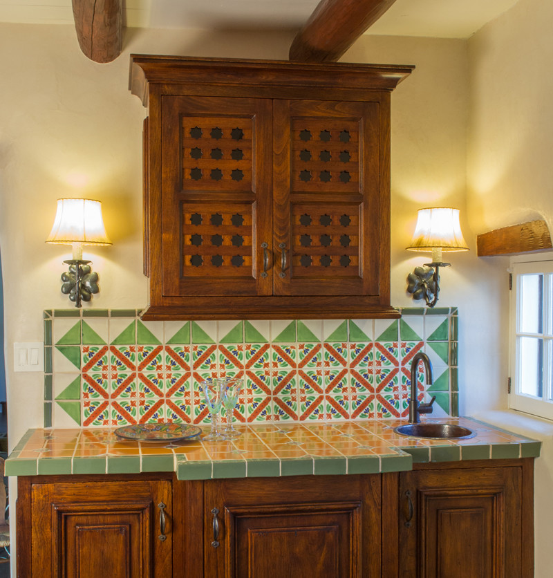Photo of a small mediterranean single-wall wet bar in Albuquerque with a drop-in sink, dark wood cabinets, tile benchtops, multi-coloured splashback and ceramic splashback.