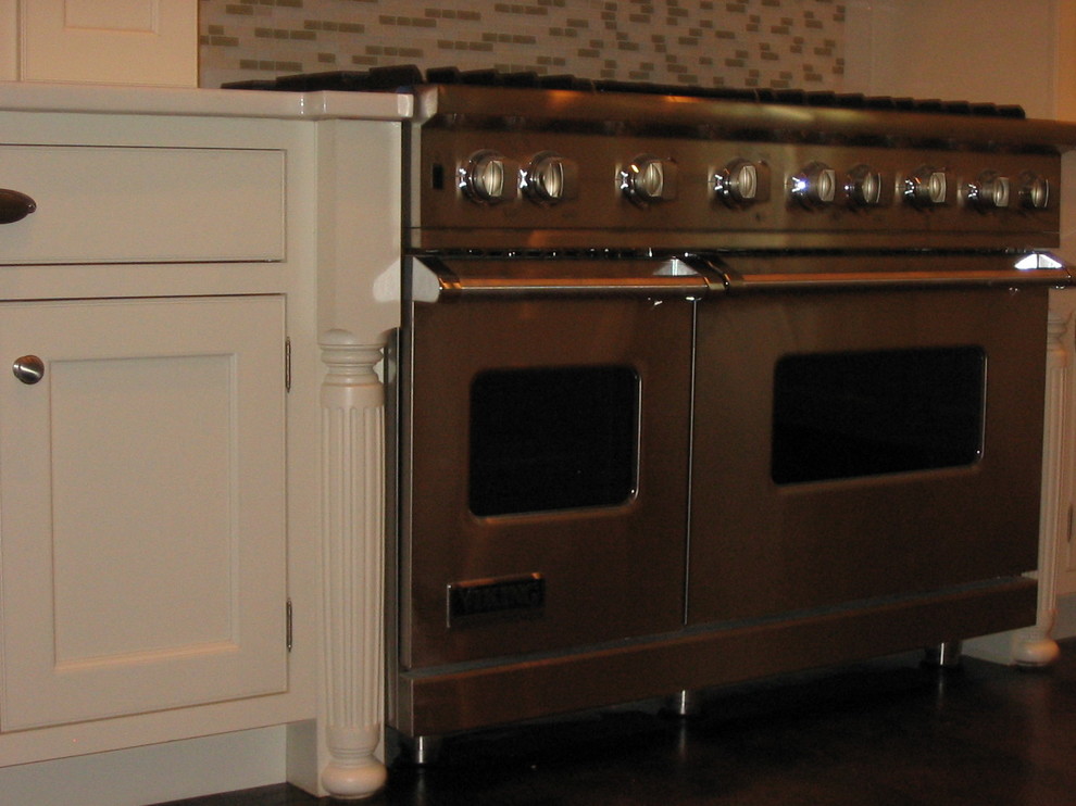 Example of a large transitional l-shaped dark wood floor and brown floor eat-in kitchen design with a drop-in sink, raised-panel cabinets, white cabinets, solid surface countertops, white backsplash, ceramic backsplash, stainless steel appliances and an island