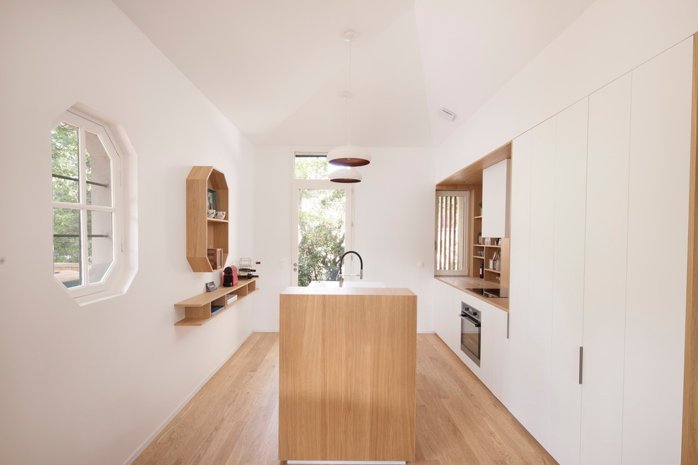 Contemporary galley kitchen in Paris with flat-panel cabinets, white cabinets, wood benchtops, stainless steel appliances, medium hardwood floors, with island, brown floor and brown benchtop.