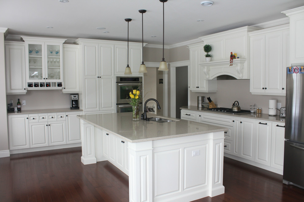Example of a mid-sized transitional l-shaped medium tone wood floor eat-in kitchen design with an undermount sink, raised-panel cabinets, white cabinets, quartz countertops, stainless steel appliances and an island