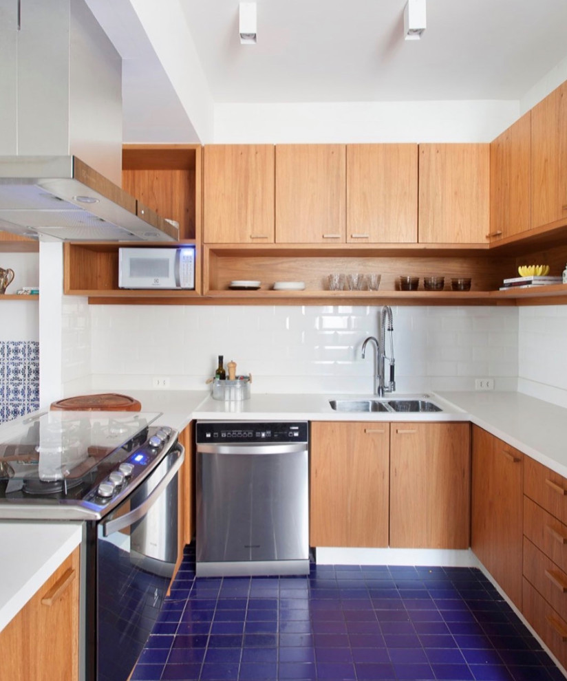 Foto på ett litet 60 tals vit l-kök, med en undermonterad diskho, släta luckor, skåp i mellenmörkt trä, bänkskiva i kvarts, vitt stänkskydd, stänkskydd i keramik, rostfria vitvaror, klinkergolv i keramik, en köksö och blått golv