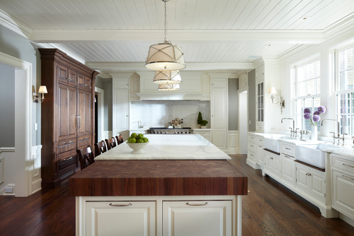 Bright traditional kitchen with white kitchen cabinets, large island with wood butcher-block and marble countertops, and tall dark wood pantry cabinet.