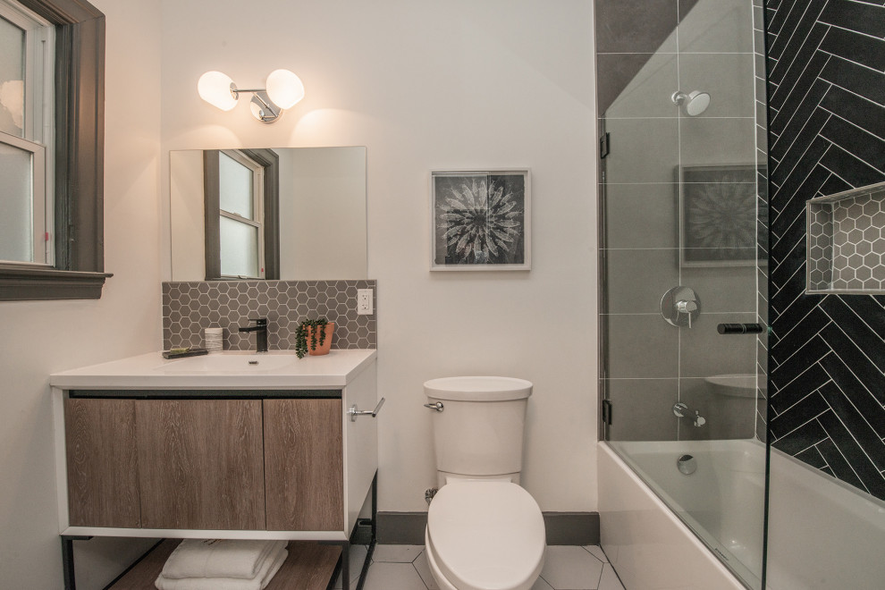 Small traditional 3/4 bathroom in Los Angeles with flat-panel cabinets, medium wood cabinets, an alcove tub, a shower/bathtub combo, a two-piece toilet, black tile, porcelain tile, white walls, porcelain floors, an integrated sink, engineered quartz benchtops, grey floor, a hinged shower door, white benchtops, a niche, a single vanity and a freestanding vanity.