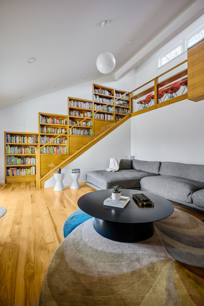 Esempio di un grande soggiorno moderno aperto con libreria, pareti bianche, pavimento in legno massello medio, TV a parete, pavimento beige e soffitto a volta