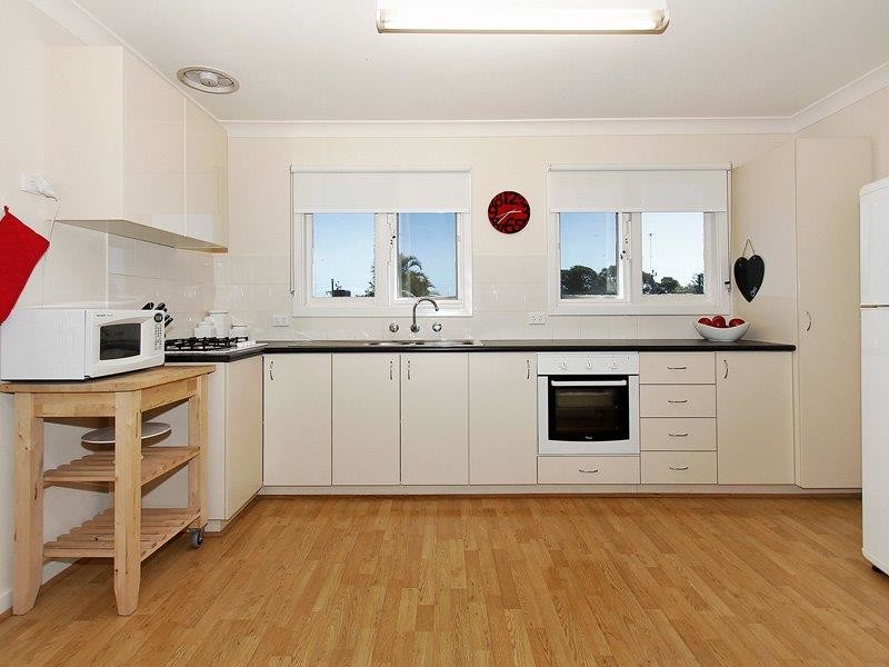 Design ideas for a small contemporary l-shaped open plan kitchen in Perth with a double-bowl sink, beige cabinets, laminate benchtops, beige splashback, ceramic splashback, white appliances, light hardwood floors and no island.