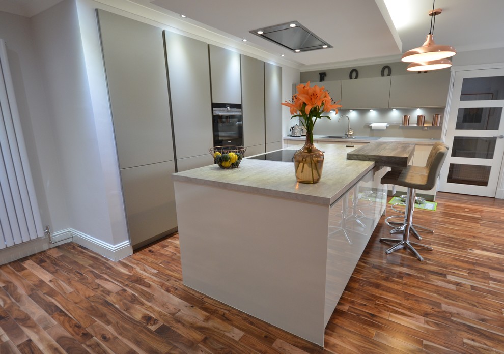 This is an example of a mid-sized contemporary galley eat-in kitchen in Other with a drop-in sink, grey cabinets, grey splashback, medium hardwood floors, with island, flat-panel cabinets, laminate benchtops, brick splashback, black appliances and brown floor.