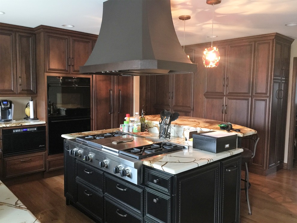 Example of a mid-sized transitional medium tone wood floor and brown floor eat-in kitchen design in Chicago with an undermount sink, raised-panel cabinets, brown cabinets, granite countertops, black appliances and an island