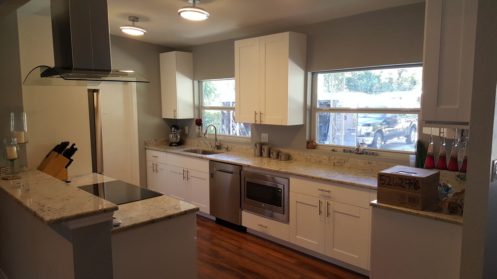 Photo of a mid-sized modern galley eat-in kitchen in Orlando with an undermount sink, shaker cabinets, white cabinets, granite benchtops, white splashback, stainless steel appliances, dark hardwood floors and no island.