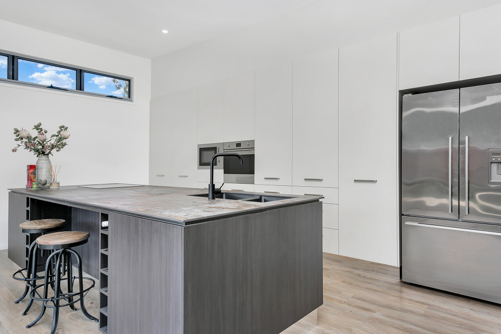 Photo of a contemporary galley kitchen in Cairns with an undermount sink, flat-panel cabinets, white cabinets, stainless steel appliances, light hardwood floors, a peninsula, beige floor and grey benchtop.