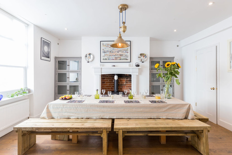 Photo of a mid-sized transitional separate dining room in Sussex with white walls, medium hardwood floors, a wood stove and a brick fireplace surround.