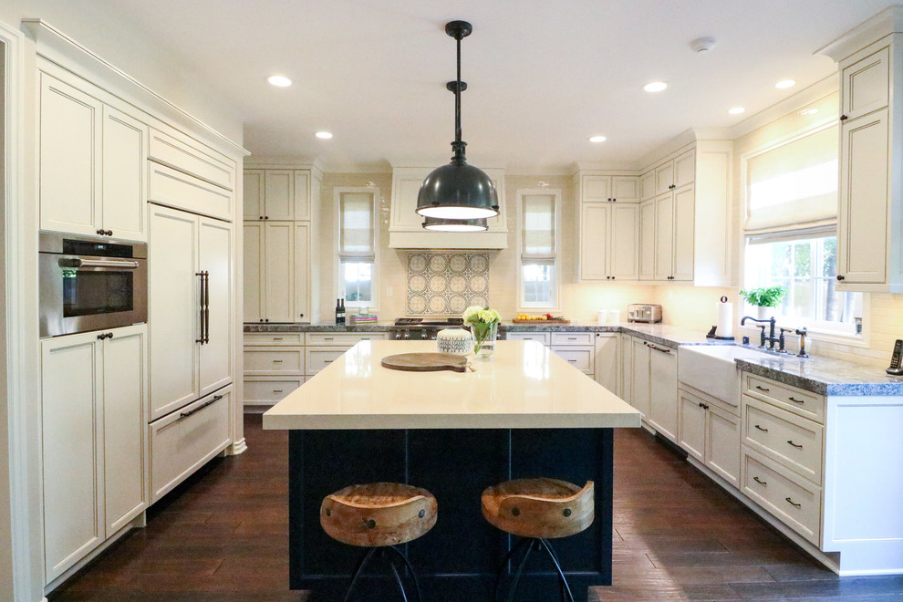This is an example of a traditional kitchen in Orange County with a farmhouse sink, recessed-panel cabinets, white cabinets, multi-coloured splashback, panelled appliances, dark hardwood floors, with island, brown floor and grey benchtop.