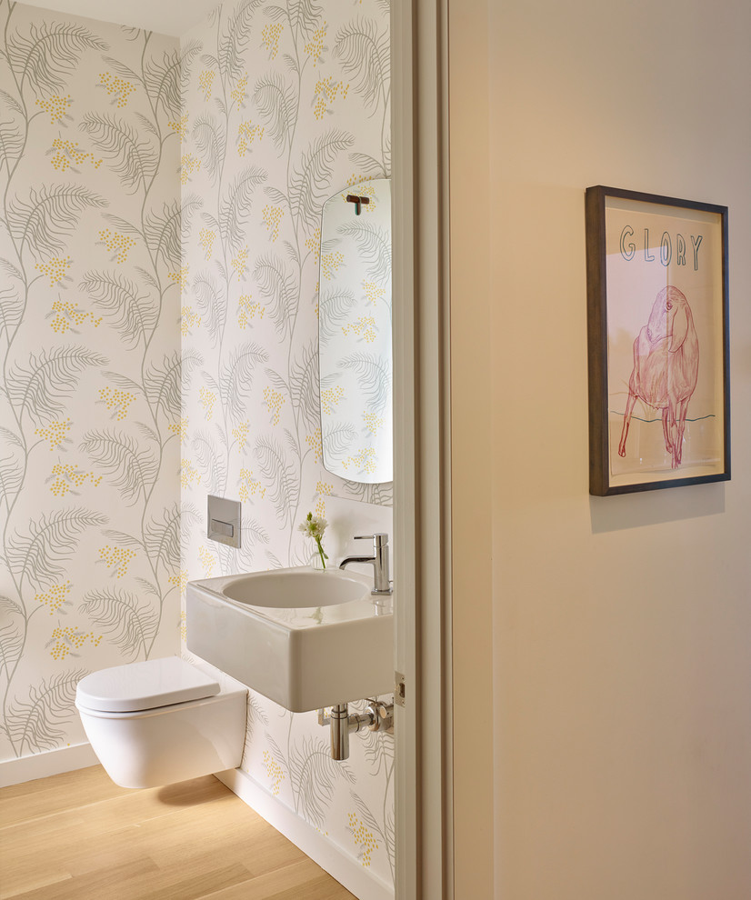 Photo of a small transitional powder room in San Francisco with a wall-mount toilet, multi-coloured walls, light hardwood floors, a wall-mount sink and beige floor.