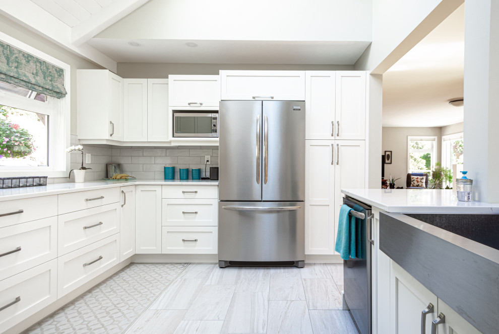 Design ideas for a mid-sized traditional u-shaped eat-in kitchen in Vancouver with a farmhouse sink, shaker cabinets, white cabinets, quartz benchtops, grey splashback, ceramic splashback, stainless steel appliances, laminate floors, with island, beige floor and white benchtop.