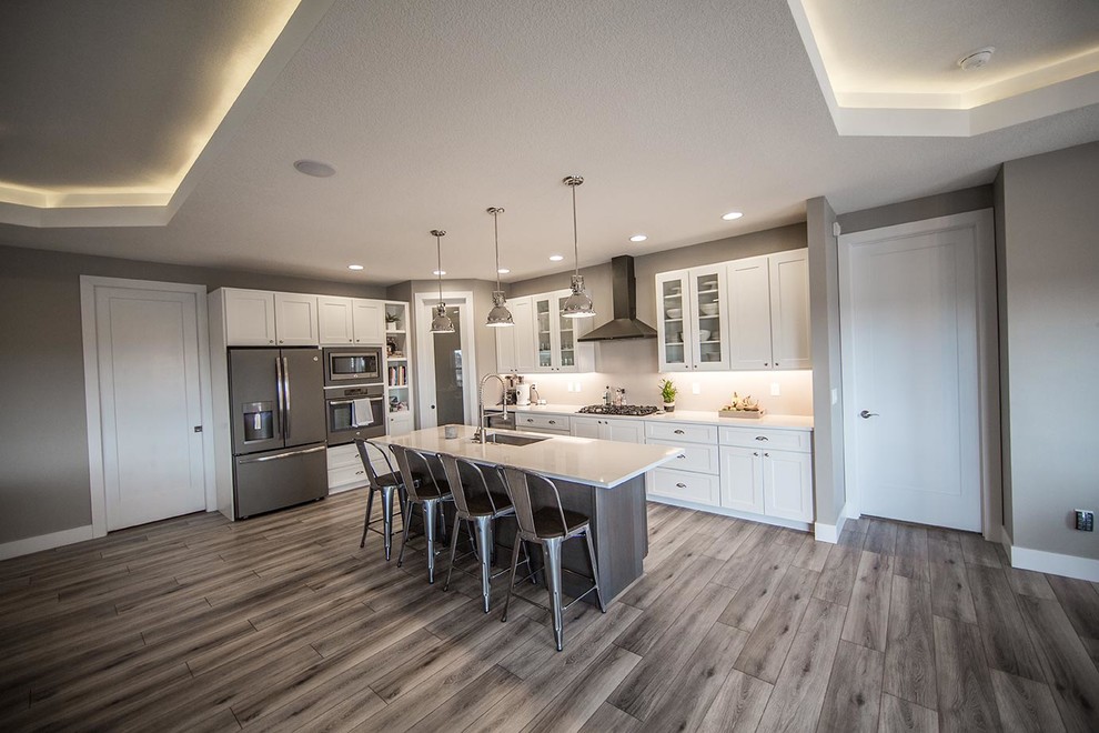 Eat-in kitchen - large transitional laminate floor and brown floor eat-in kitchen idea in Cedar Rapids with a farmhouse sink, shaker cabinets, white cabinets, quartzite countertops, stainless steel appliances and an island