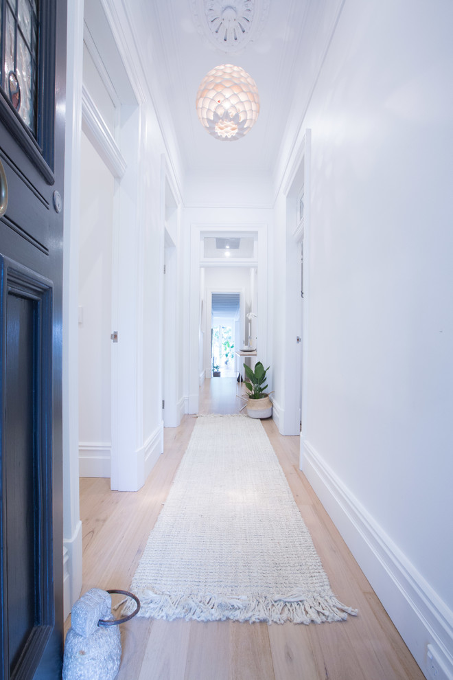 Design ideas for a mid-sized beach style hallway in Sydney with white walls and light hardwood floors.