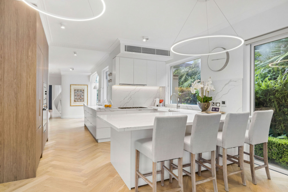 Contemporary u-shaped kitchen in Sydney with a farmhouse sink, flat-panel cabinets, white cabinets, white splashback, light hardwood floors, a peninsula, beige floor and white benchtop.
