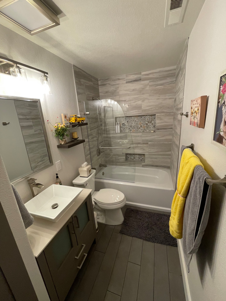 Photo of a mid-sized transitional bathroom in San Francisco with furniture-like cabinets, grey cabinets, a drop-in tub, an alcove shower, a two-piece toilet, multi-coloured tile, porcelain tile, beige walls, porcelain floors, an undermount sink, engineered quartz benchtops, grey floor, a hinged shower door, multi-coloured benchtops, a niche, a double vanity and a freestanding vanity.