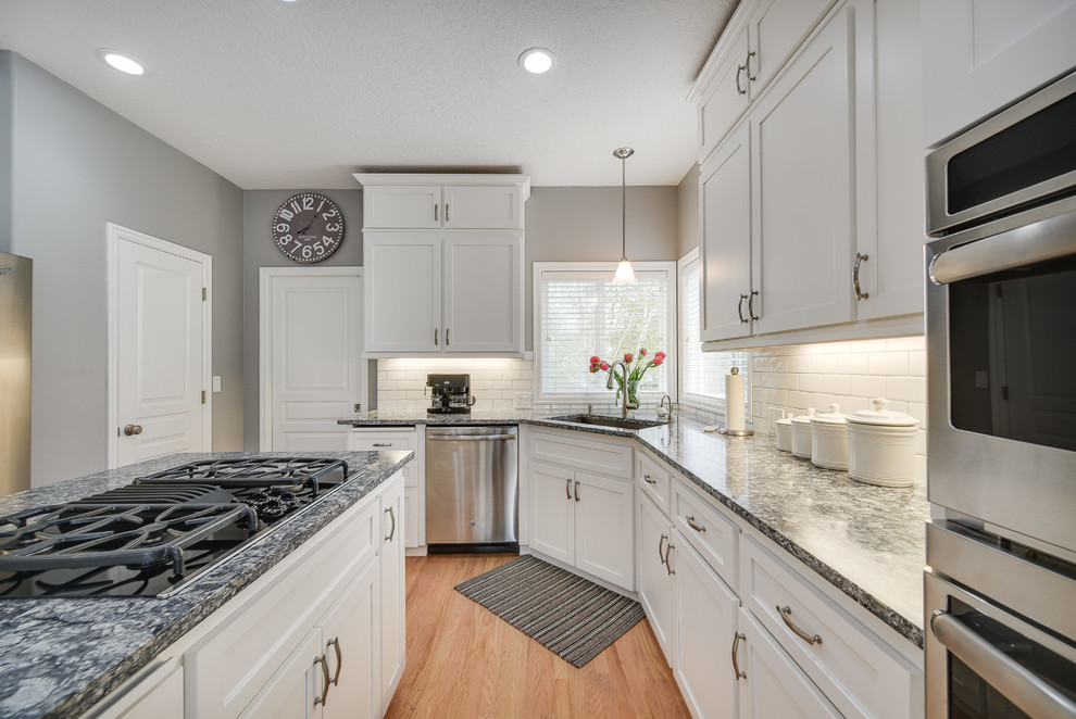 Enclosed kitchen - mid-sized transitional l-shaped light wood floor and brown floor enclosed kitchen idea in Portland with a drop-in sink, shaker cabinets, white cabinets, quartz countertops, white backsplash, subway tile backsplash, an island and stainless steel appliances