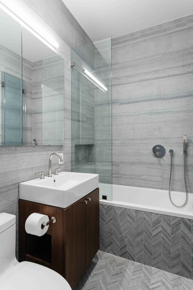 This is an example of a mid-sized contemporary bathroom in New York with flat-panel cabinets, a drop-in tub, marble, marble floors, marble benchtops, grey floor, dark wood cabinets, a shower/bathtub combo, a one-piece toilet, gray tile, a console sink, an open shower, a niche, a single vanity and a built-in vanity.