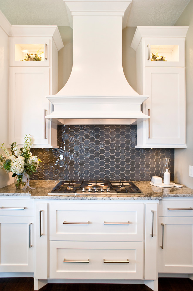 Eat-in kitchen - mid-sized transitional l-shaped medium tone wood floor and brown floor eat-in kitchen idea with raised-panel cabinets, white cabinets, granite countertops, gray backsplash, glass tile backsplash, paneled appliances and an island
