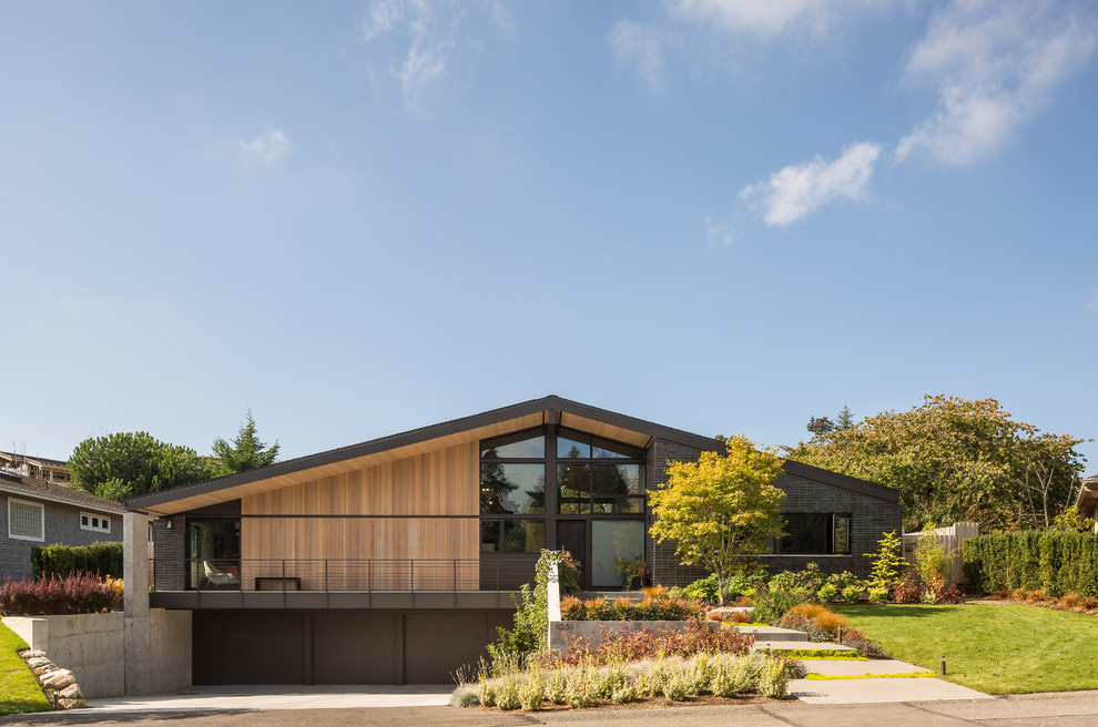 Large midcentury two-storey black exterior in Seattle with a gable roof and mixed siding.