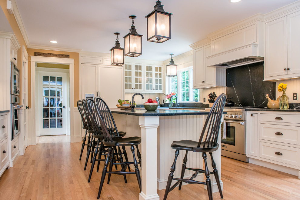 This is an example of a mid-sized transitional u-shaped eat-in kitchen in Portland Maine with an undermount sink, shaker cabinets, white cabinets, stainless steel appliances, bamboo floors and with island.