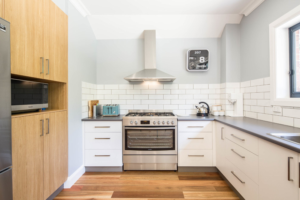 Inspiration for a mid-sized transitional u-shaped eat-in kitchen in Canberra - Queanbeyan with a drop-in sink, flat-panel cabinets, white cabinets, laminate benchtops, white splashback, porcelain splashback, stainless steel appliances, medium hardwood floors, beige floor and no island.