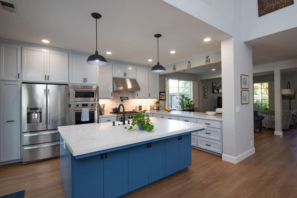 Modern inredning av ett grå grått kök och matrum, med en undermonterad diskho, skåp i shakerstil, blå skåp, bänkskiva i kvarts, vitt stänkskydd, stänkskydd i keramik, rostfria vitvaror och en köksö