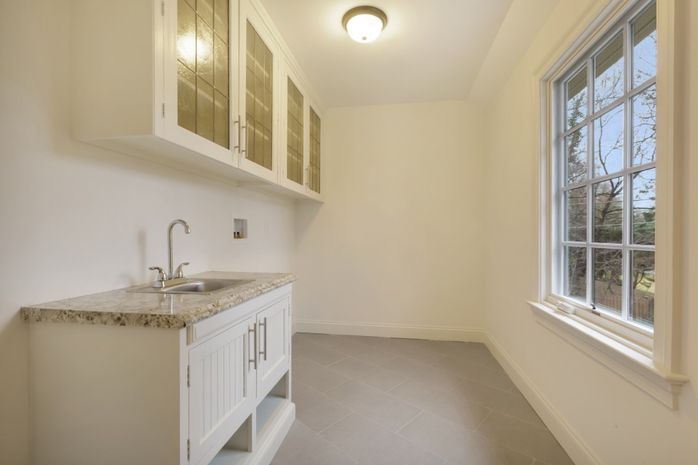 Photo of a mid-sized contemporary dedicated laundry room in Philadelphia with a drop-in sink, glass-front cabinets, white cabinets, laminate benchtops, white walls, porcelain floors, a side-by-side washer and dryer, grey floor and grey benchtop.