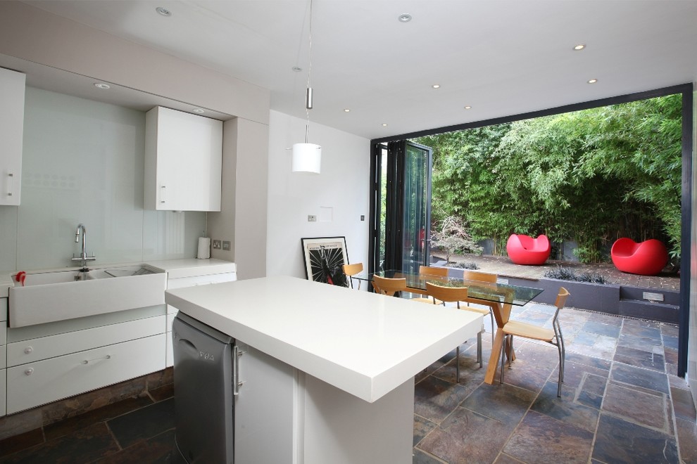 Inspiration for a contemporary eat-in kitchen in London with a farmhouse sink, flat-panel cabinets, white cabinets, white splashback, glass sheet splashback and stainless steel appliances.