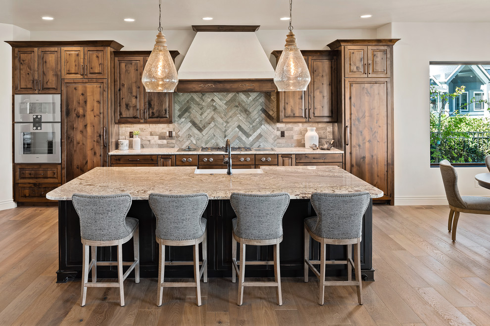 Design ideas for a traditional eat-in kitchen in Boise with a farmhouse sink, raised-panel cabinets, medium wood cabinets, granite benchtops, grey splashback, ceramic splashback, stainless steel appliances, with island, light hardwood floors and beige benchtop.