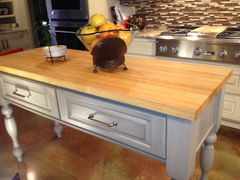Eat-in kitchen - mid-sized eclectic galley concrete floor eat-in kitchen idea with a farmhouse sink, raised-panel cabinets, white cabinets, granite countertops, brown backsplash, glass tile backsplash, stainless steel appliances and an island